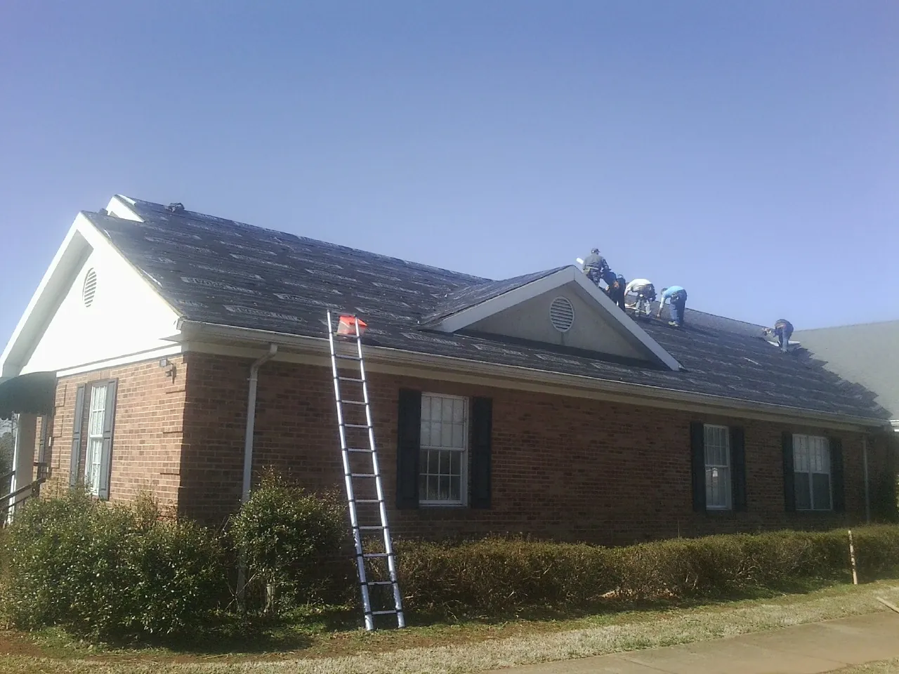Crew tearing shingles off a brick ranch roof with a ladder set — Emergency Roof Repair work by our crew in Fowler