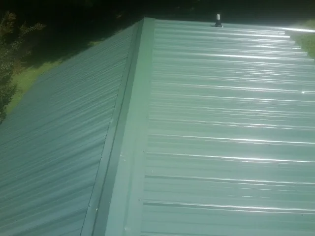 New green metal panels meeting at the ridge of a roof — Flat Roof Repair work by our crew in Fowler