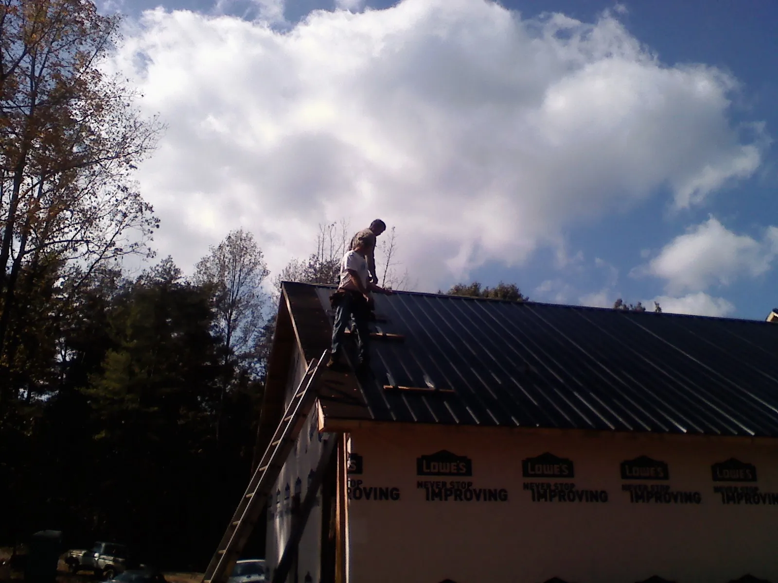 Roofer fastening dark metal panels high against a cloudy sky, from a Roof Inspection job in Fowler